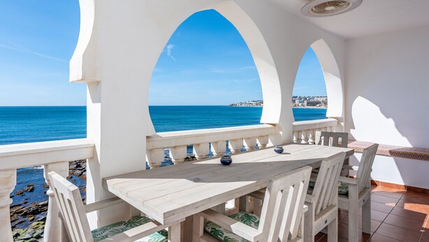 Una terraza con mesa y sillas, con vistas a la costa.