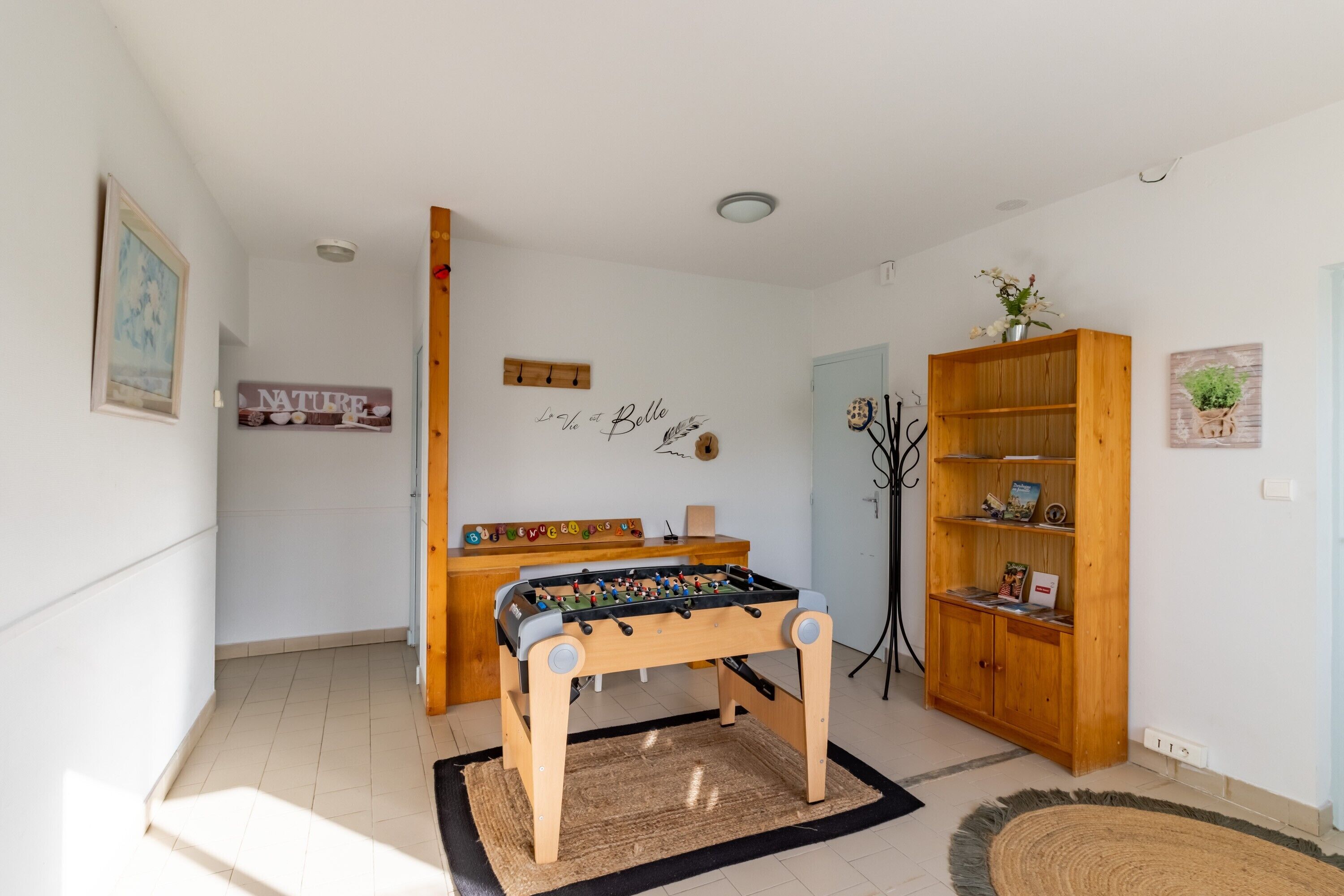 Una habitación con mesa de fútbol, un mueble de madera, un cuadro enmarco y un cartel en la pared.