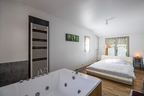 Un dormitorio moderno con una cama grande, una bañera integrada y un ventanal con cortinas.