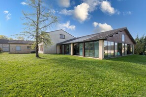 Una casa moderna con un amplio ventanal de vidrio, un jardín con césped y un cielo azul despejado.