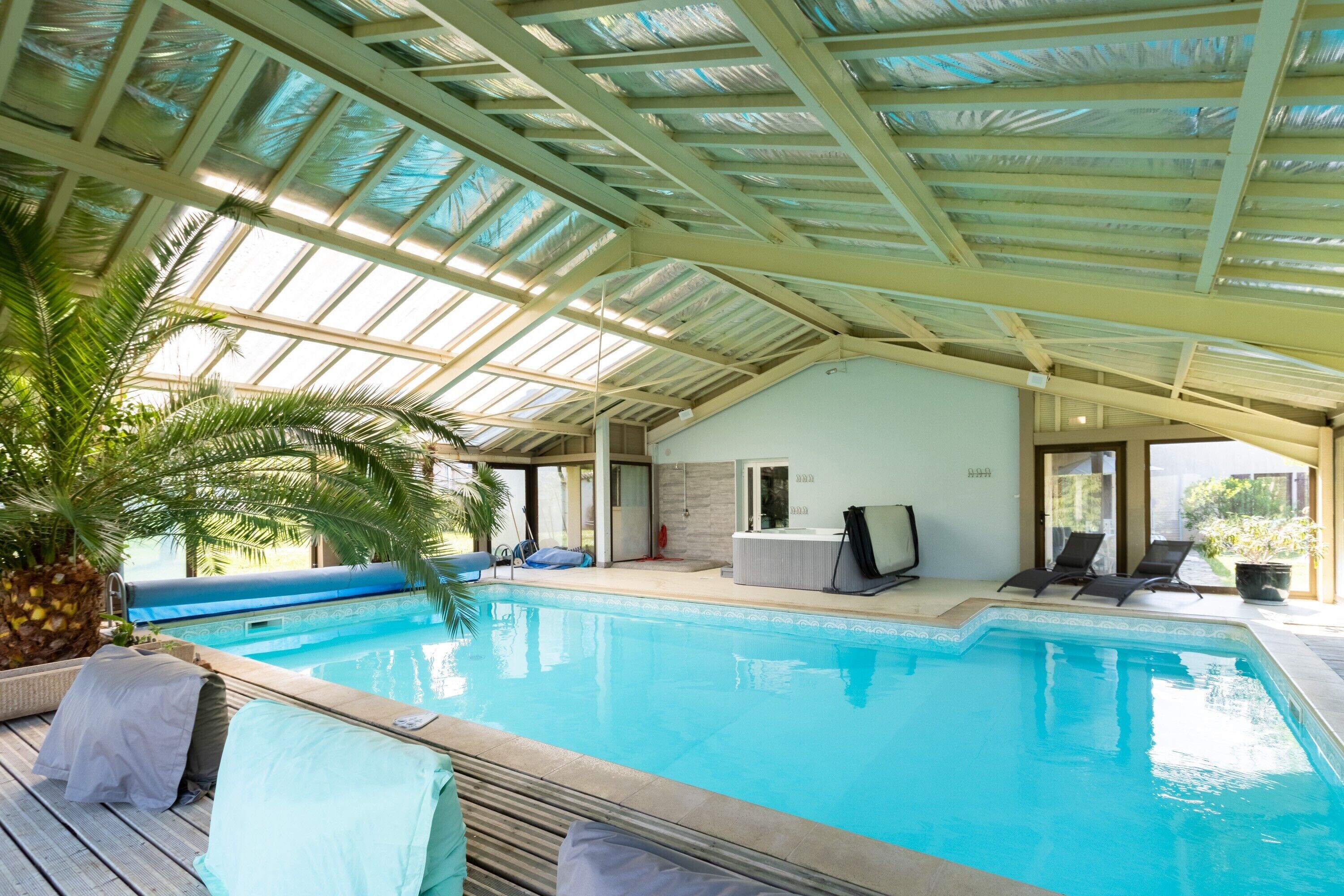 Une piscine intérieure dotée d’un toit en verre, de chaises longues et d’un petit espace salon.