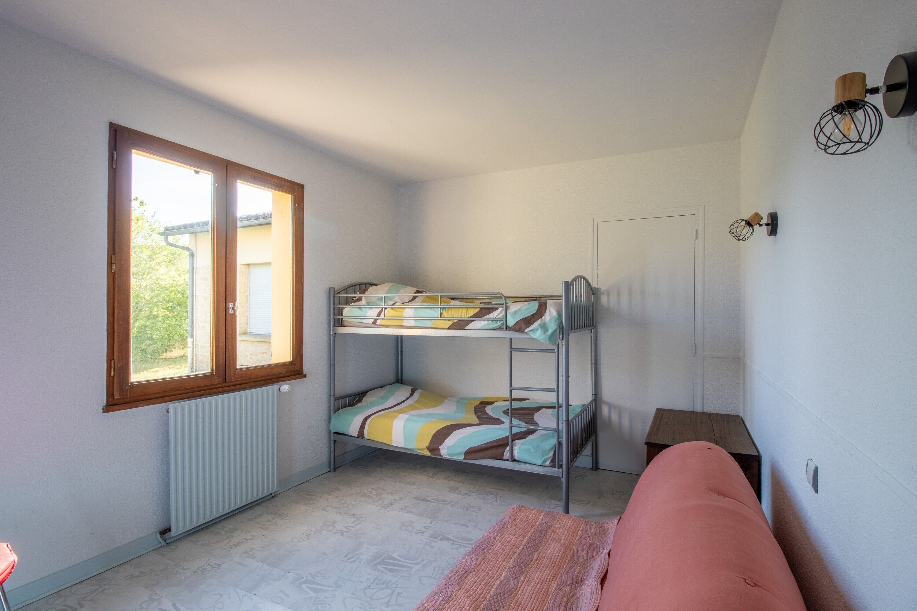 A room with a bunk bed, a radiator, a window, a door, and a small table.