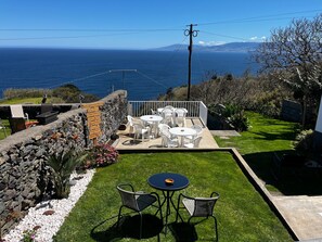 Un patio con sillas y mesas blancas, un muro de piedra y vistas al océano.