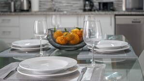 Une table à manger dressée avec de l’assiette blanche, des verres à vin transparents et un saladier rempli de fruits.