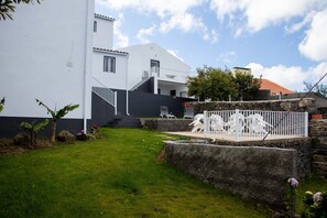 Un edificio de dos pisos con fachada blanca, un muro de contención de piedra y un patio cubierto de césped.