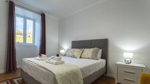 Un lit bien fait, avec des oreillers et une couverture, une table de chevet avec une lampe, une chaise et une fenêtre avec des rideaux.