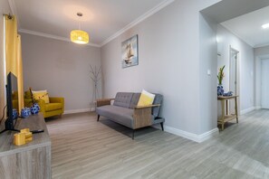 Een moderne woonkamer met een grijze bank, een geel fauteuil, een vloerlamp en een schilderij aan de muur.