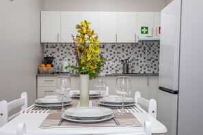 Een eethoek met een tafel gedekt voor vier personen, witte stoelen, een vaas met bloemen en een keuken op de achtergrond.