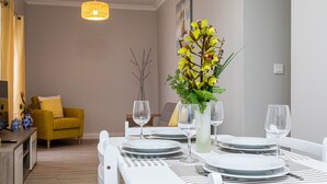 A dining area with a table set for four, a yellow armchair, a vase with flowers, and a hanging light fixture. - Apartment "Oásis Fonte Grande 4" with Sea View, Terrace & Wi-Fi (Santo António)