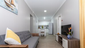 A modern living room with a sofa, a TV, and a dining area in the background. - Apartment "Oásis Fonte Grande 4" with Sea View, Terrace & Wi-Fi (Santo António)