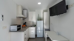Una cocina compacta equipada con microondas, lavamanos, armarios, refrigerador y un televisor de pantalla plana montado en la pared.