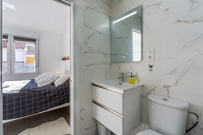 Une chambre à coucher avec un lit, une salle de bain avec un lavabo, un miroir et des toilettes.