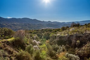Paisaje montañoso con cielo despejado, un valle con vegetación y un pueblo distante.