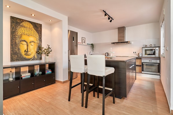 A modern kitchen with a central island, bar stools, a Buddha painting, and built-in appliances.