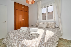 A bedroom with a bed, a wooden wardrobe, a window with curtains, and a small plant on the bedside table.