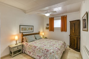 A bedroom with a bed, nightstands, a ceiling fan, a window with curtains, and a cabinet.