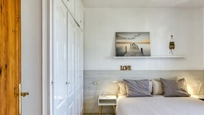 Un dormitorio con cama, mesita de noche, estante en la pared y un cuadro.