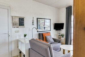 Un salon moderne avec un canapé, une petite table, un téléviseur et une fenêtre avec des rideaux.