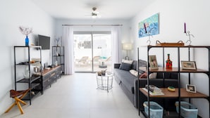 Un salon moderne avec un canapé, un téléviseur, des étagères et une vue sur l’extérieur.