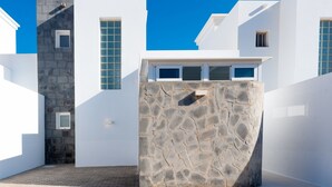 Un bâtiment moderne de couleur blanche, doté d’un mur en pierre, d’une petite fenêtre et d’une porte.