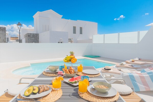 Área de piscina en la azotea con zona de comedor, que incluye platos de comida, bebidas y una presentación de frutas.