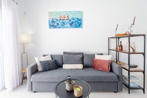 Una sala moderna con un sofá gris, una mesa redonda de centro, un cuadro en la pared y una estantería con libros y velas.