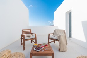 Un balcón con dos sillas de madera, una mesa con un frutero y vasos, y vista al cielo.