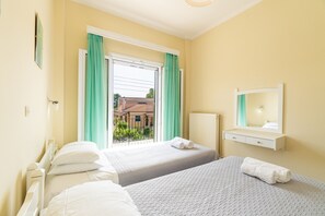 A hotel room with two beds, a window with curtains, a radiator, and a mirror above the bed.