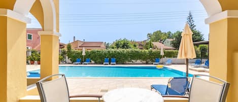 Ein Poolbereich mit Stühlen und einem Tisch, mit freiem Blick auf den Pool sowie eine gelbe Gebäudefassade.