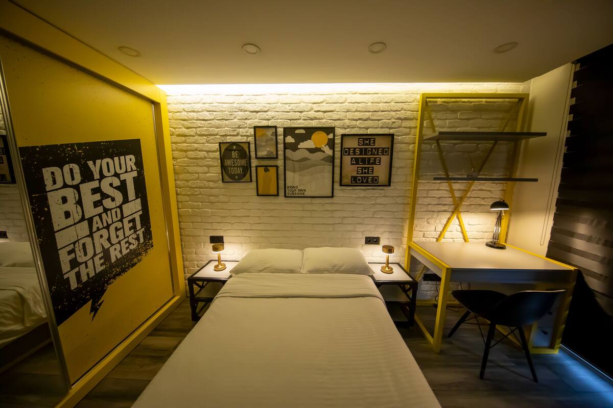 Un dormitorio con cama, dos mesitas de noche con lámparas, un escritorio con silla y carteles decorativos en la pared.