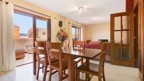 A dining area with a wooden table and chairs, a vase with flowers, and a view through the glass door.