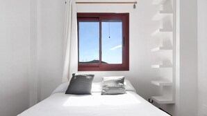 A bedroom with a bed, two pillows, a window with curtains, and a white wall.
