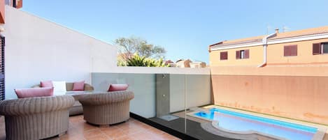 A rooftop terrace with a swimming pool, wicker furniture, and a view of neighboring buildings.