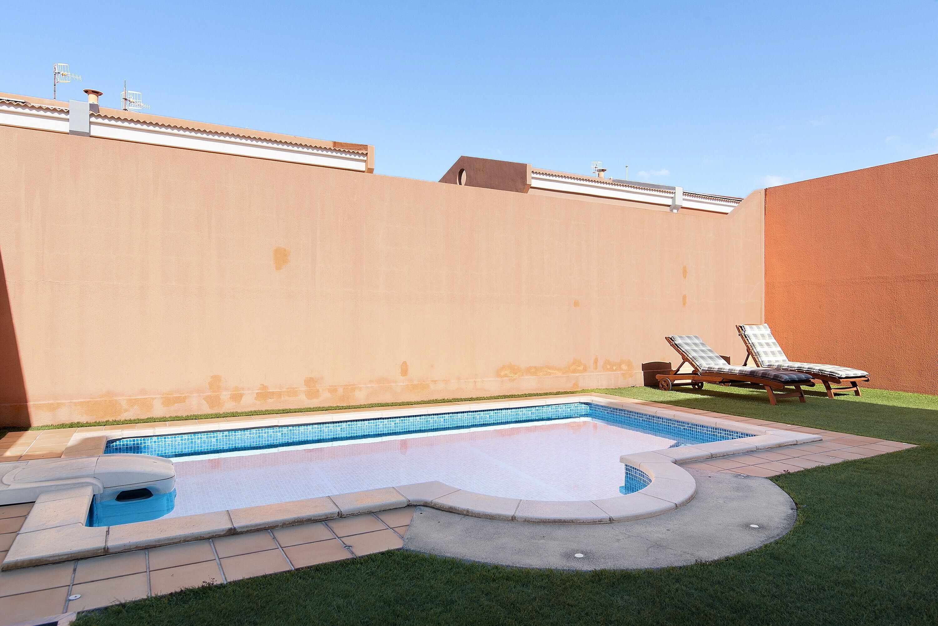 Ein Pool mit gefliestem Deck, zwei Liegestühlen und einer kleinen Whirlwanne.
