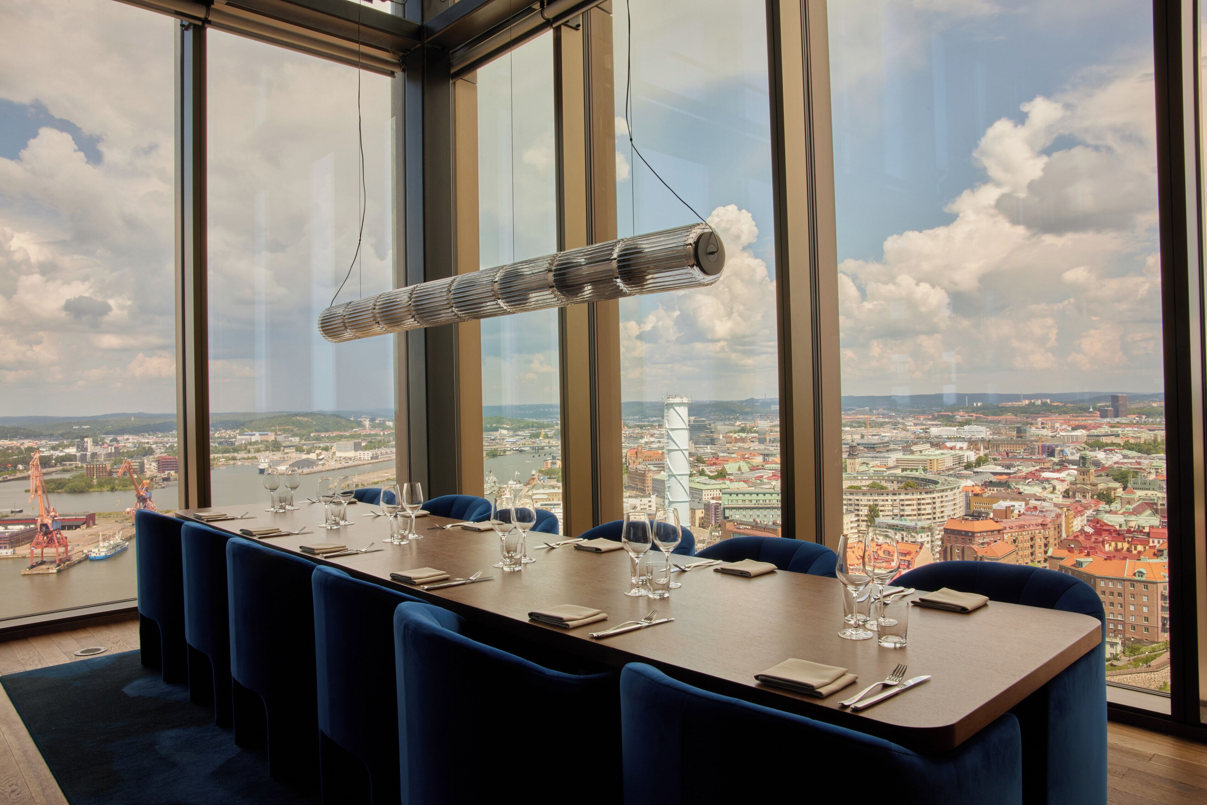 A dining area with a table set for six, large windows offering a city view, and a hanging light fixture.