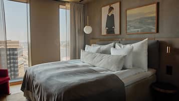 A modern hotel room with a large bed, a view of the city, and two framed pictures on the wall.