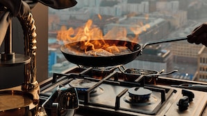 Una cocina con vista a un paisaje urbano, una estufa con una sartén y una persona cocinando.