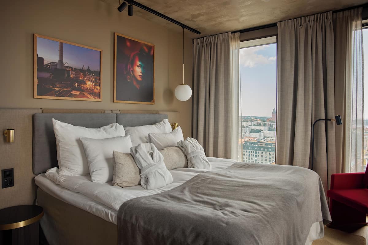 Una habitación de hotel moderna con una cama grande, vistas a la ciudad y dos cuadros en la pared.