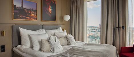 Una habitación de hotel moderna con una cama grande, vistas a la ciudad y dos cuadros en la pared.