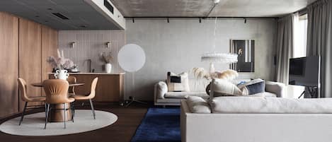 Una sala de estar moderna con un sofá, una mesa de comedor con sillas, una zona de cocina y un amplio ventanal con cortinas.
