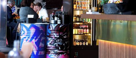 A bar area with a counter, seating, and a refrigerated display of beverages.