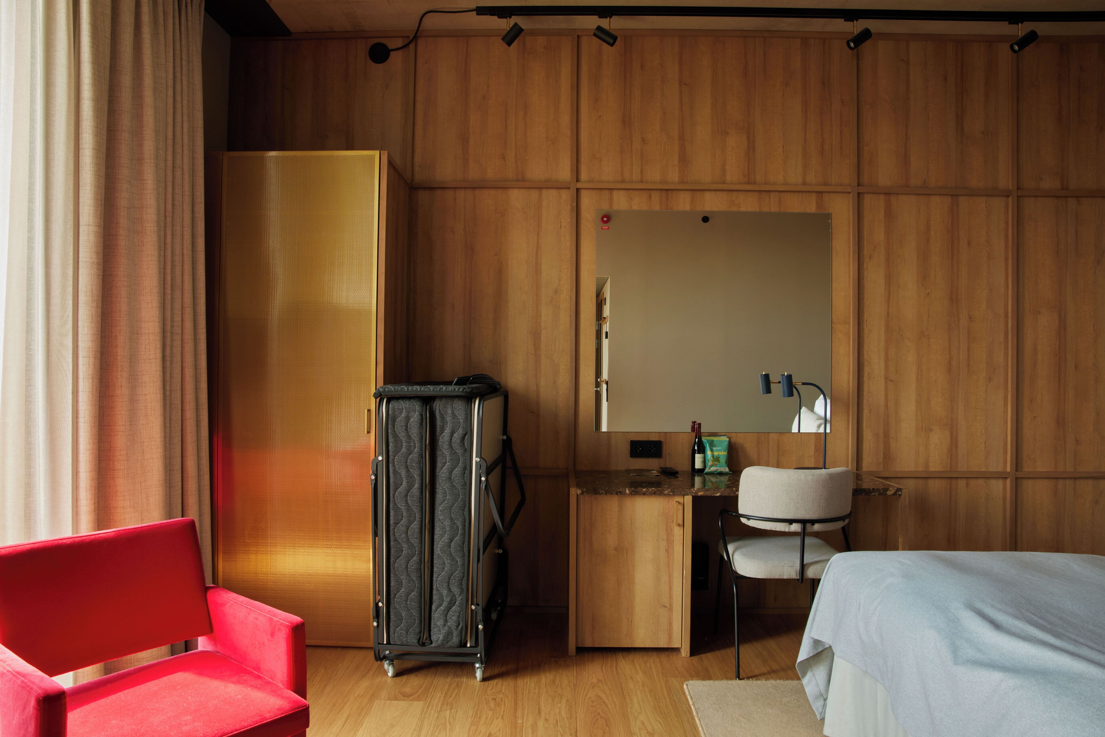 Una habitación de hotel con un armario de madera, un escritorio con espejo, una silla roja y una cama.