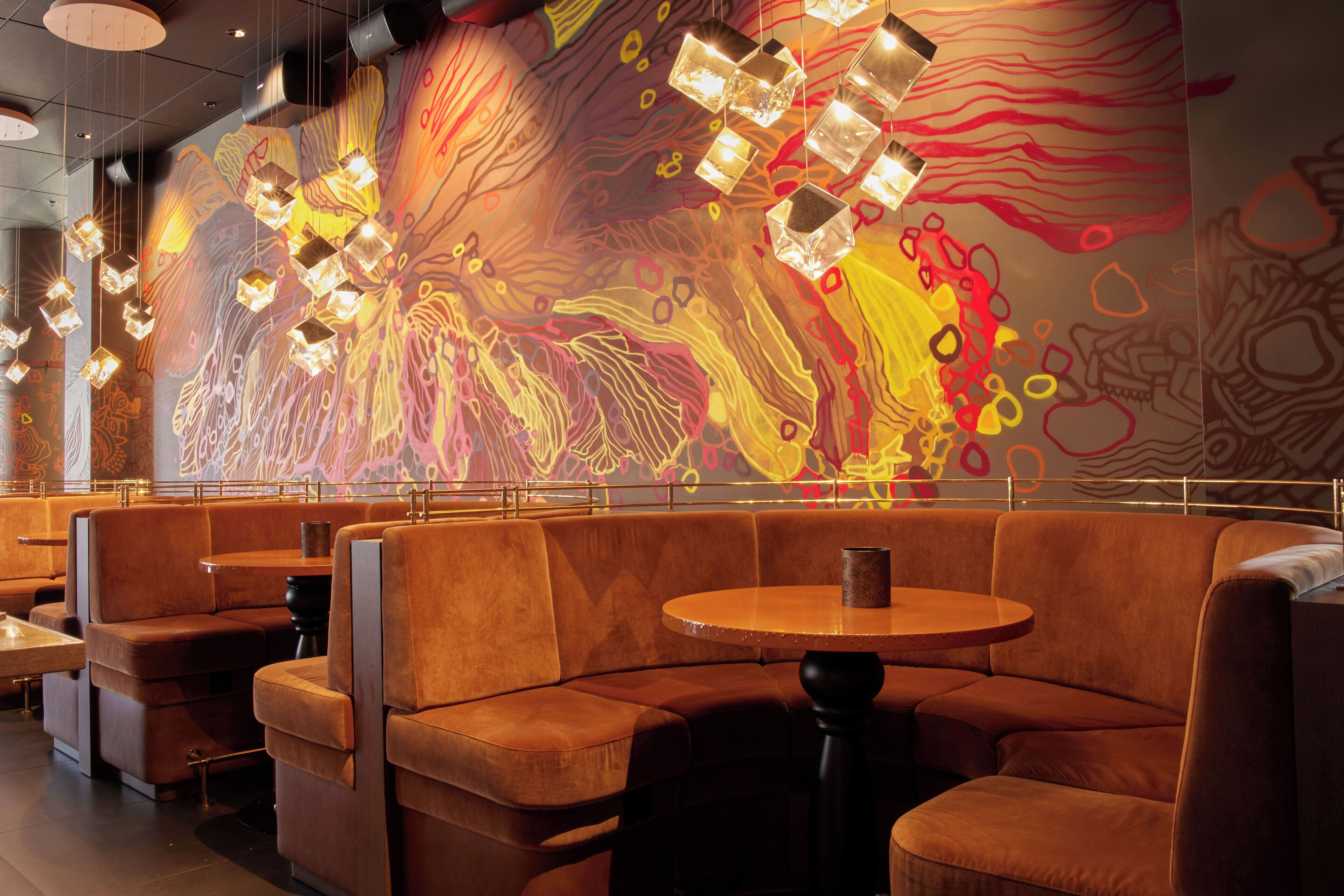 A restaurant with booth seating and a colorful abstract mural on the wall.