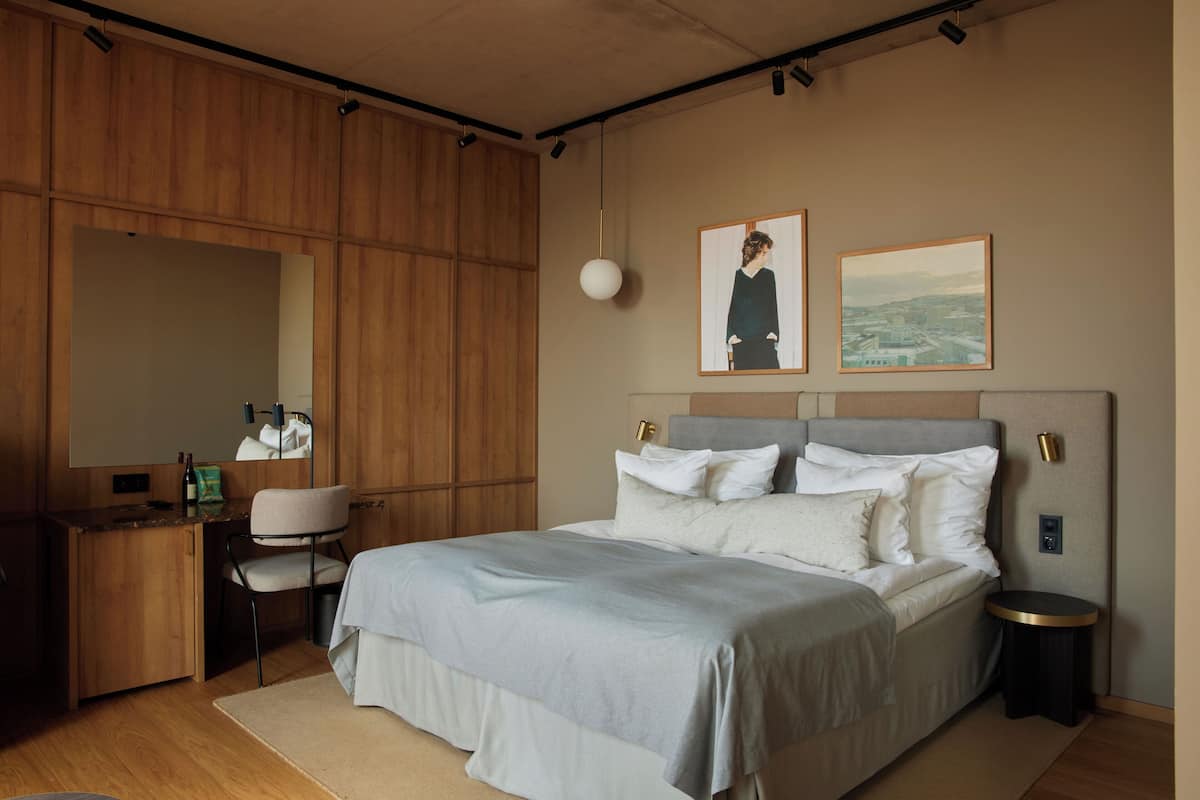 Un dormitorio moderno con una cama grande, un escritorio y una silla. Hay dos cuadros en la pared.