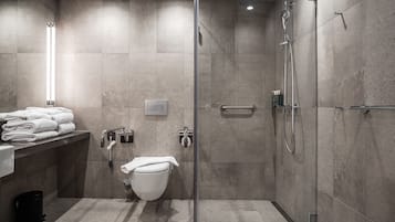 A modern bathroom with a glass-enclosed shower, a toilet, and a sink area with towels.