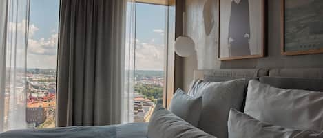 A hotel room with a large bed, a sofa, and a city view through the window.