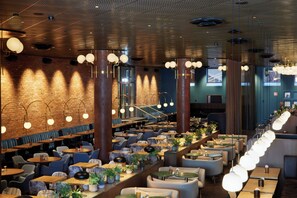 Een ruim restaurant met hoge plafonds, zichtbare bakstenen muren en verschillende zitmogelijkheden, zoals zitbanken en tafels.