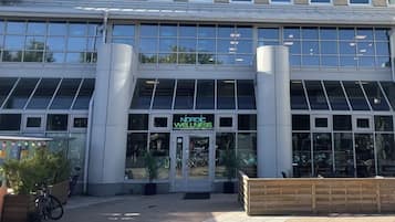 Um edifício moderno com fachada de vidro, um letreiro com a inscrição 'Nordic Wellness' e um banco de madeira na parte externa.
