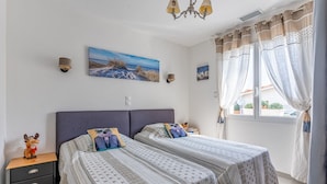A bedroom with two beds, a nightstand, a wall-mounted lamp, and a window with curtains. - Beautiful Villa 500 m from the Lake with Pool and Air Conditioning (Gastes)