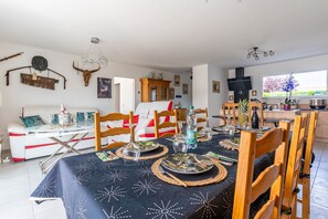A dining area with a table set for four, chairs, a sofa, and a kitchen in the background.